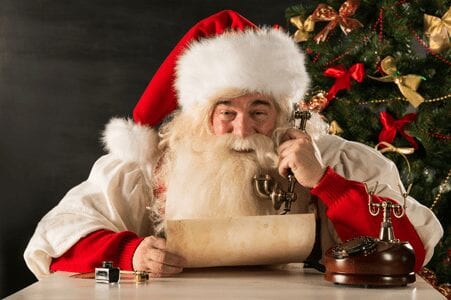 Weihnachtsmann mit altem Telefonhörer in der Hand, der eine Schriftrolle liest und lacht